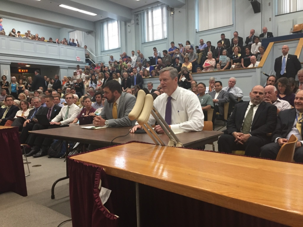 Gov. Charlie Baker, with crutches, testifies sitting next to Secretary of Energy and Environmental Affairs Matthew Beaton in crowded Gardner Auditorium at the State House.
