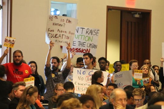 Protesters hold up signs during the speech by state Education Secretary James Peyser.